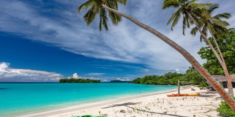 Beach scene in Vanuatu with a kayak on the sand and palm trees.