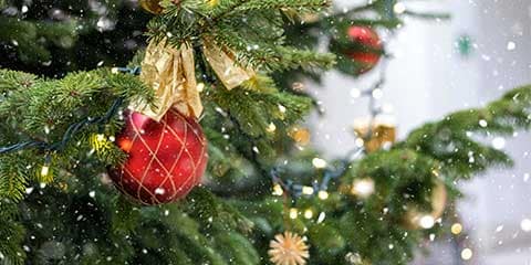 snow falling on decorated Christmas tree with red bauble