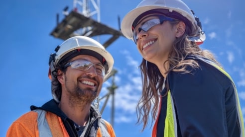 male and female Optus employees wearing hard hats with a network tower in background