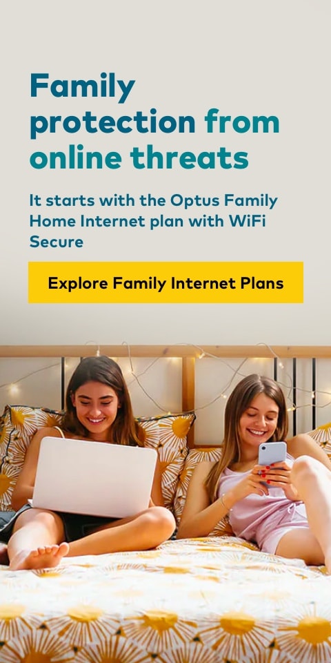 two girls smiling at a laptop and phone while laying in bed
